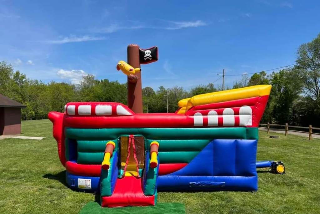 A bright red and blue inflatable bounce house stands in a sunny backyard, filled with laughing kids